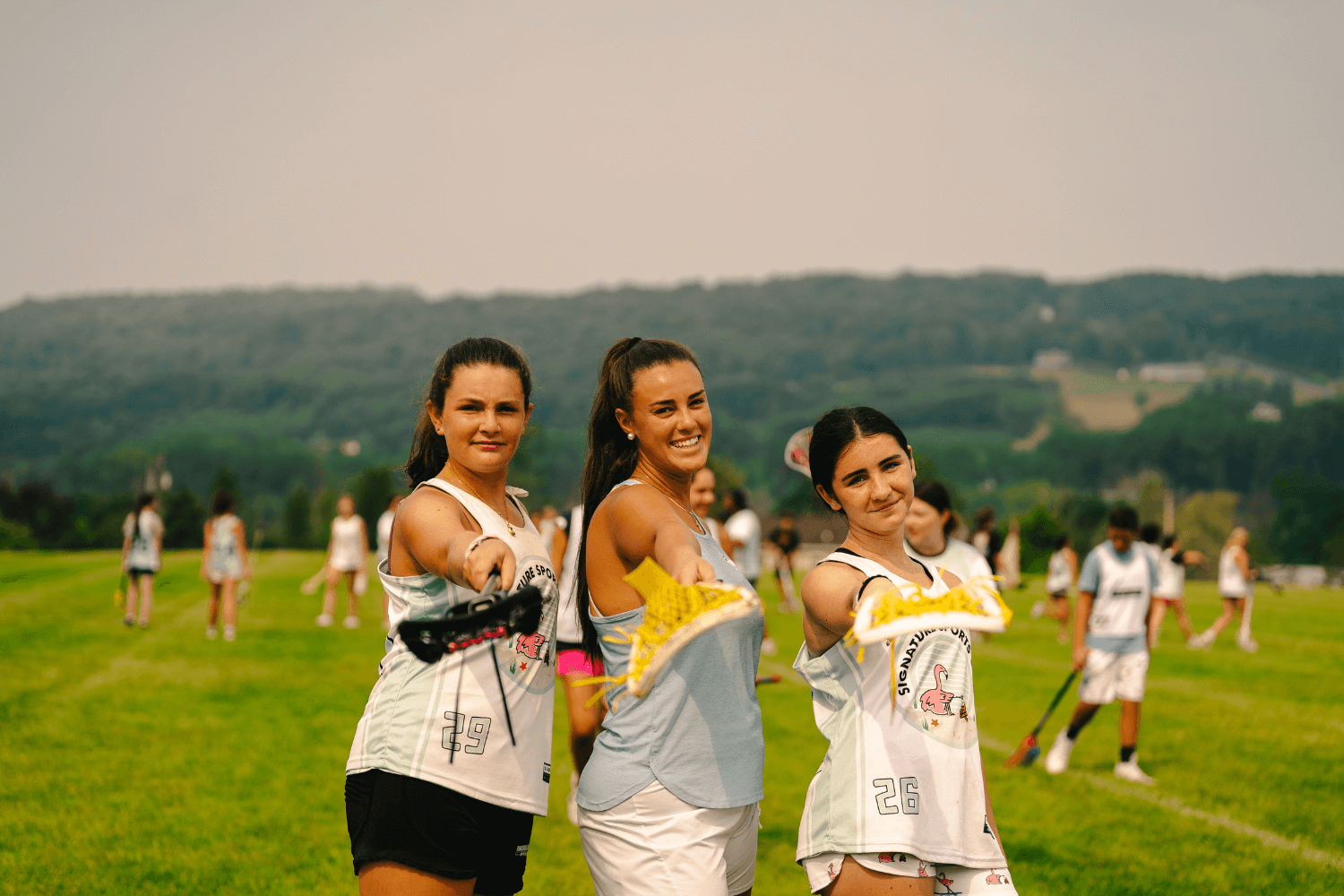 Three girls holding lacrosse sticks up while posing for a photo at Signature Sports Camps