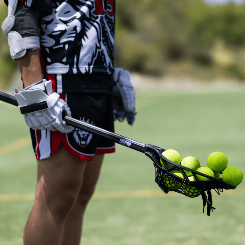 Boy wearing lacrosse uniform is holding a lacrosse stick that is overflowing with yellow signature lacrosse balls