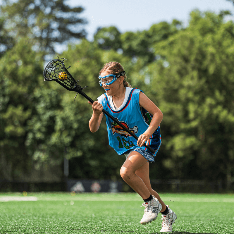 young girl in lacrosse uniform holding a lacrosse stick and ball during practice